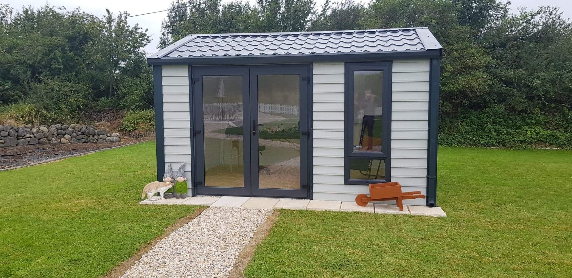 Small shed with glass doors and a window, next to a gravel path and a grassy yard.