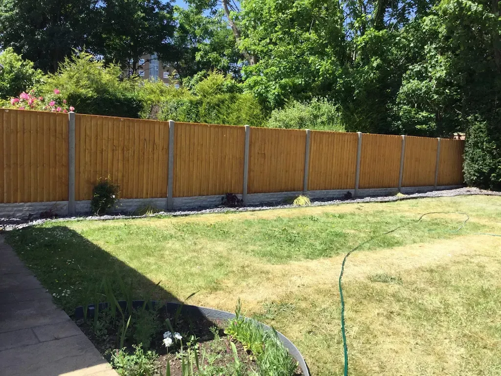 Wooden fence in a backyard, with a lawn in the foreground and trees in the background.