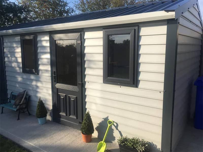 Gray shed with dark gray door, windows, and trim; concrete patio, garden decor.