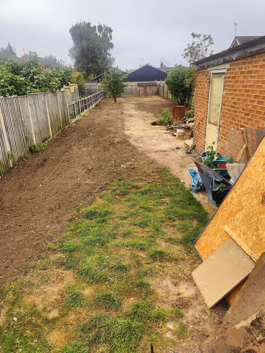 Long backyard with freshly tilled soil, a grassy area, and a wooden fence along the side.