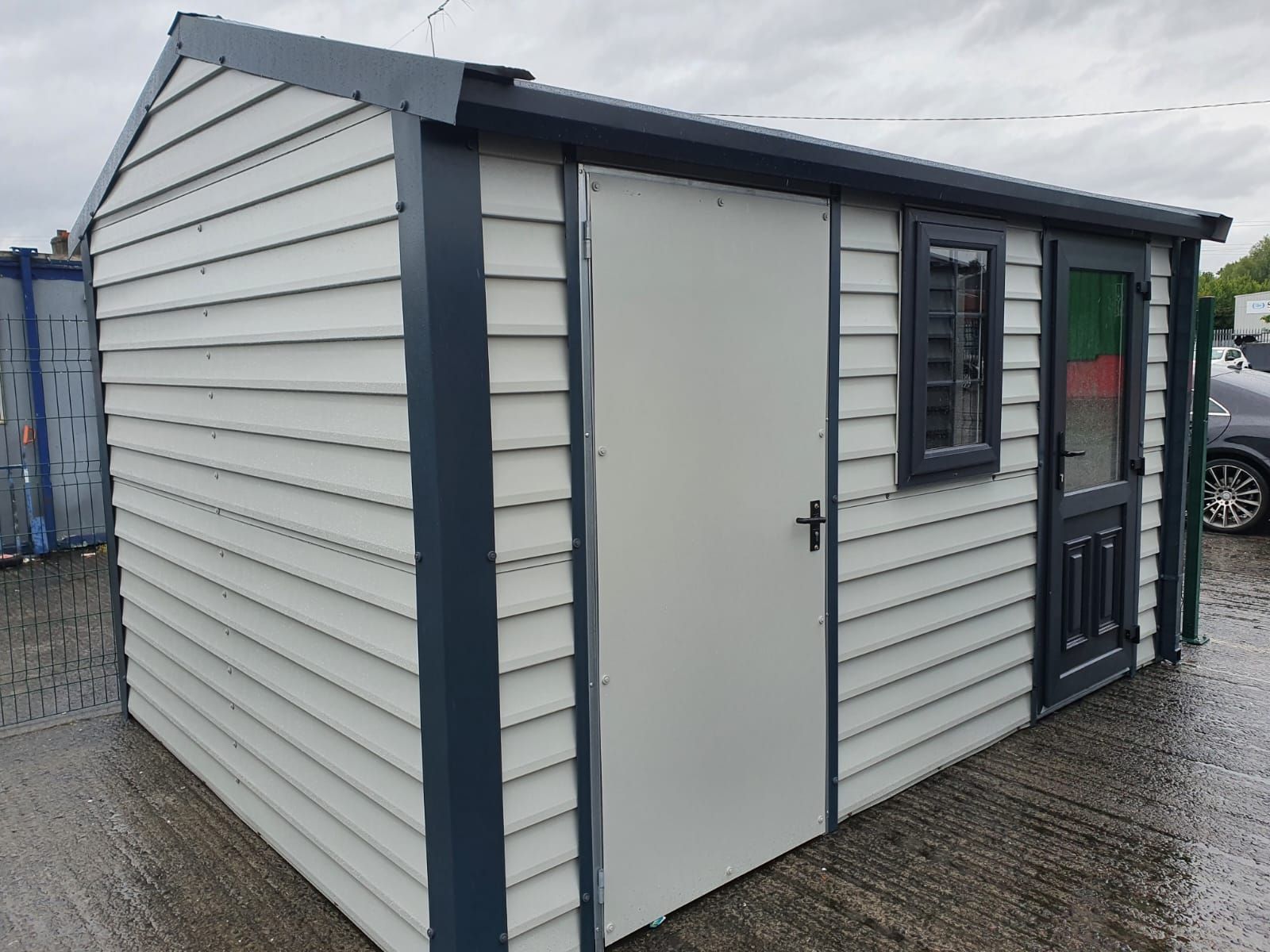 Gray and white shed with a white door and window, dark trim, outdoors.