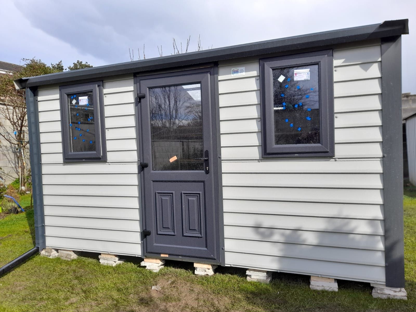 Gray and white shed with a door and two windows on a grassy lawn.