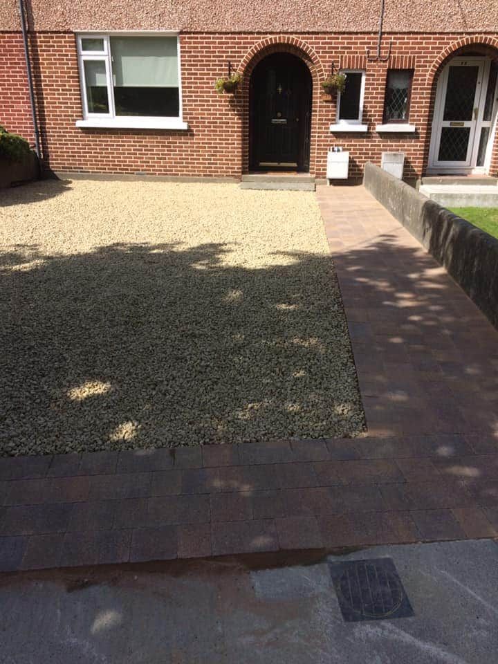 Brick house front with gravel driveway, grass patch, and brick pathway leading to the arched doorway.