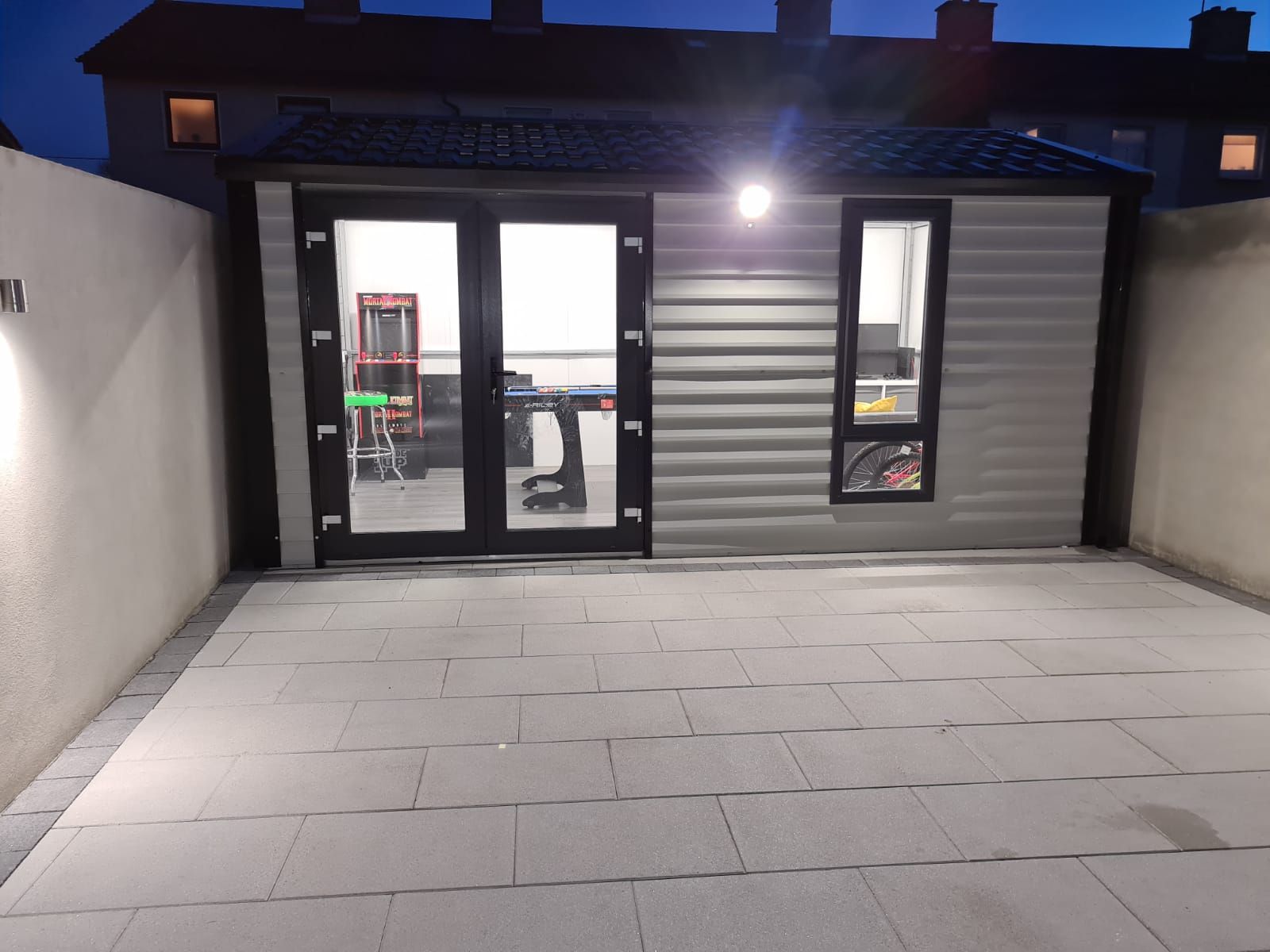 Backyard patio with a shed at night, lit by spotlights.