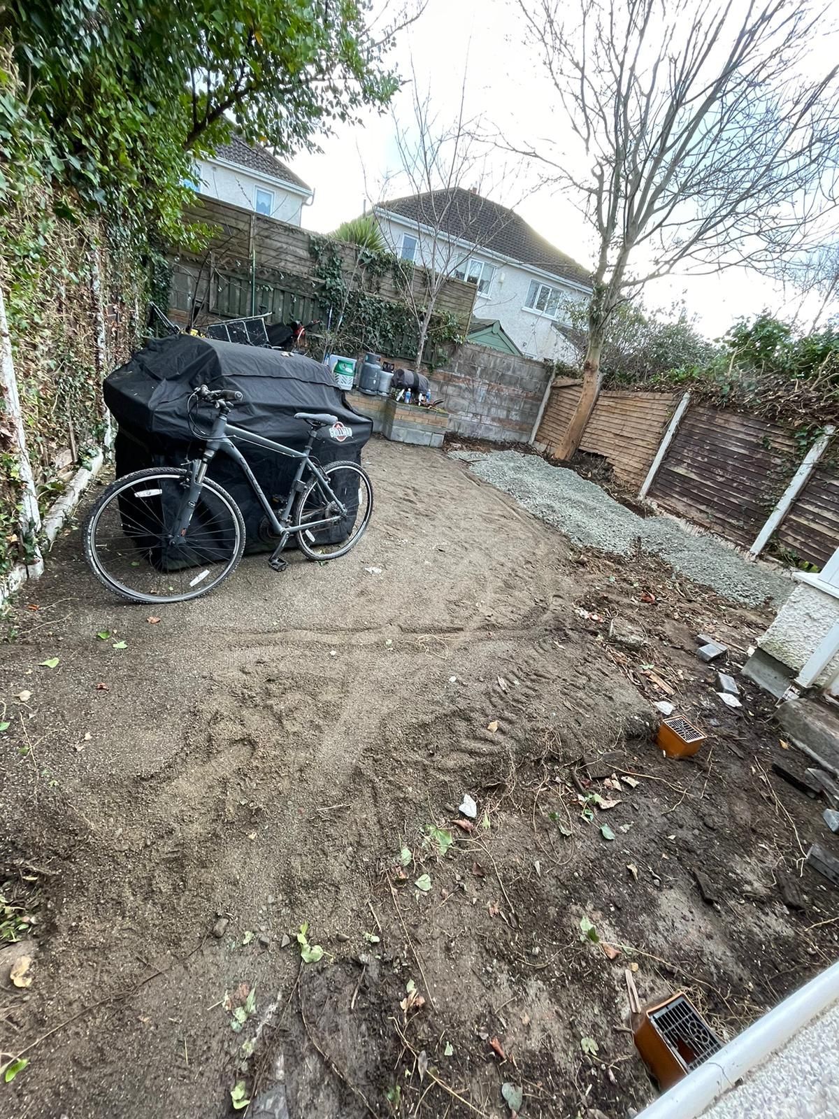 Dirt backyard with a black bike, black objects, fence, and houses in the background.