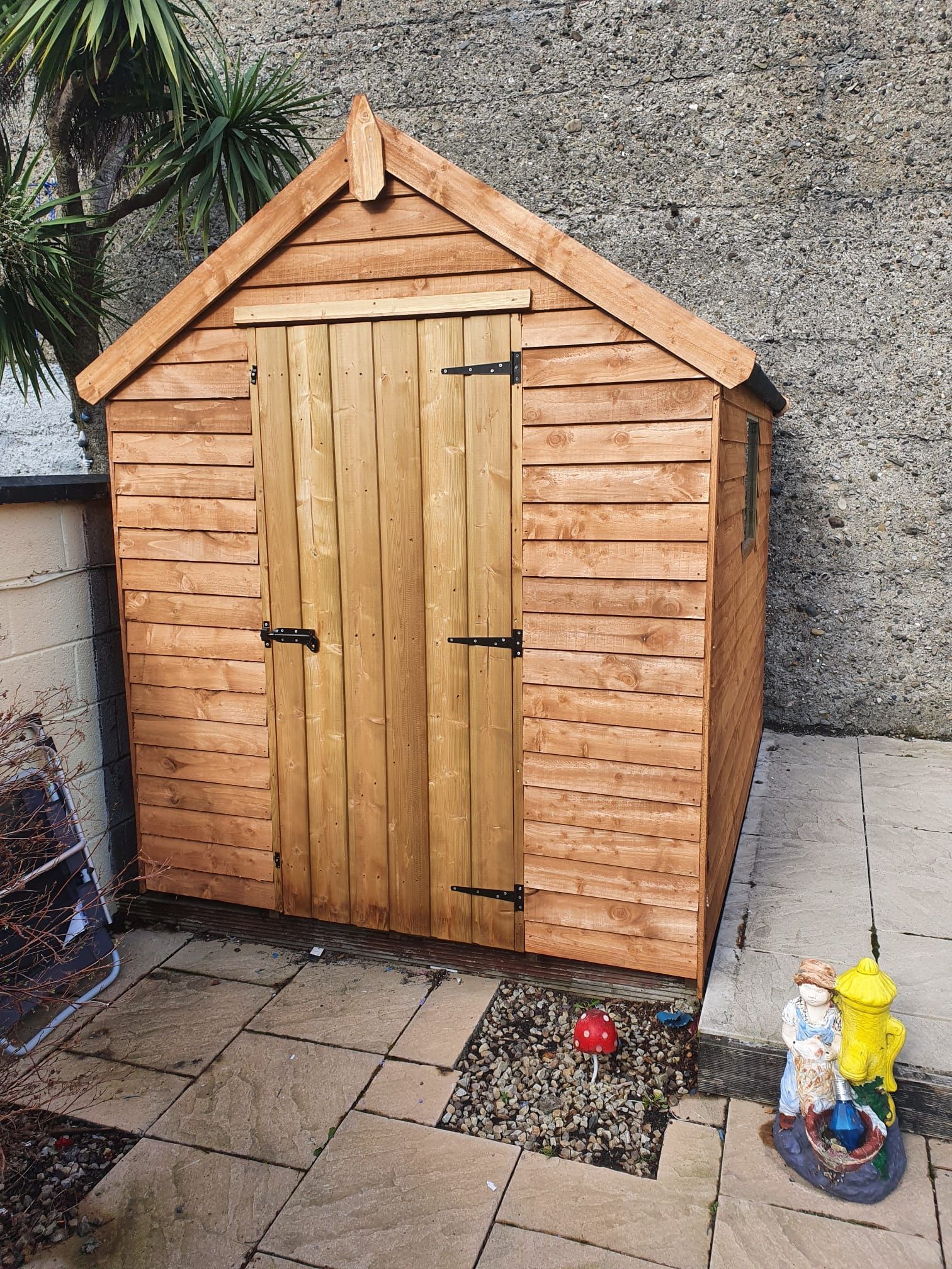 Wooden shed with a pitched roof and double doors in a paved yard.