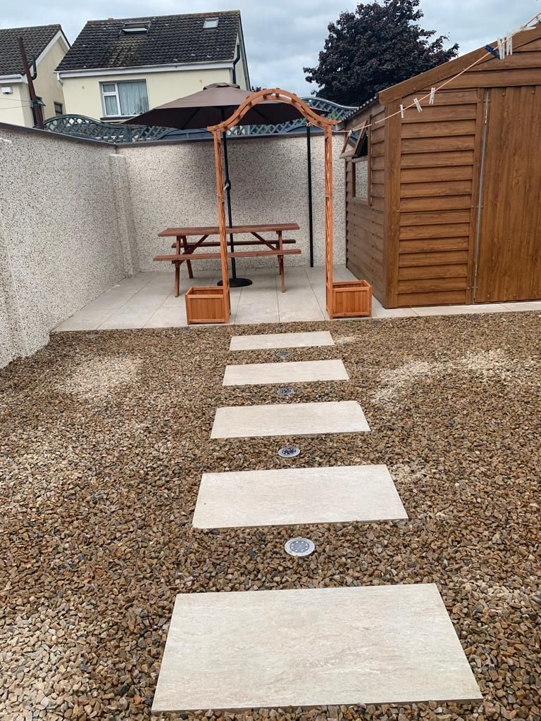 Stone path through gravel yard leads to a picnic table and wooden arch.
