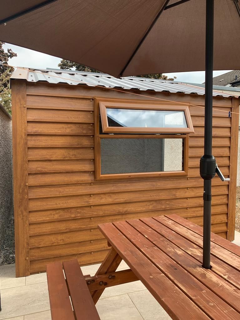 Wooden shed with open window and brown picnic table. Brown umbrella shades table.