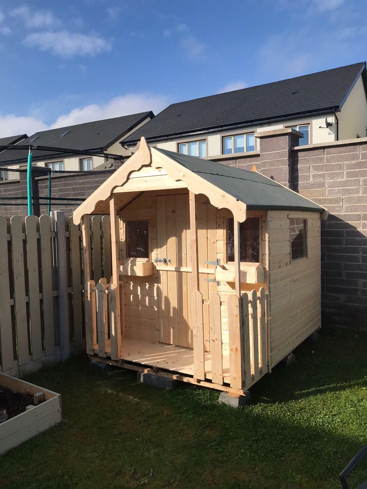 Wooden playhouse in a backyard with a picket fence and a brick wall.