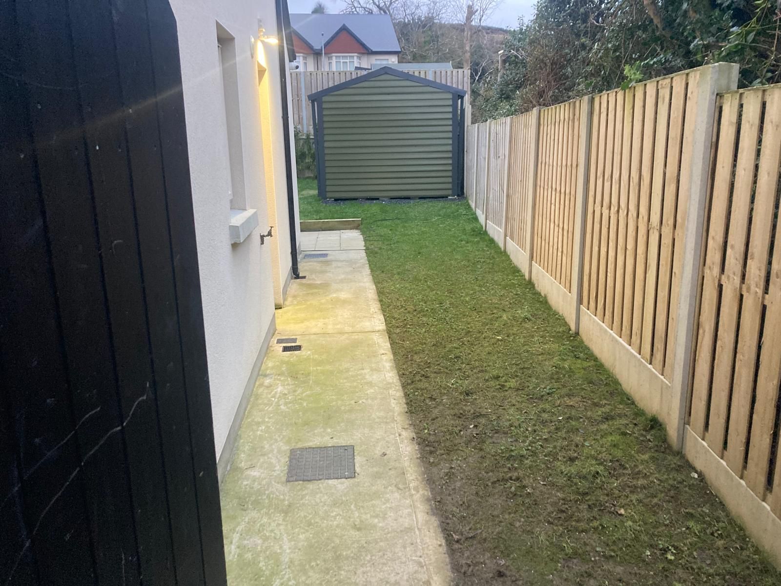 Narrow backyard with concrete path, grass, wooden fence, and shed.
