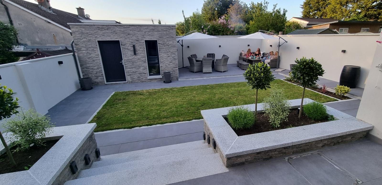Modern backyard with patio, lawn, and raised garden beds. A building with a black door is on the left.