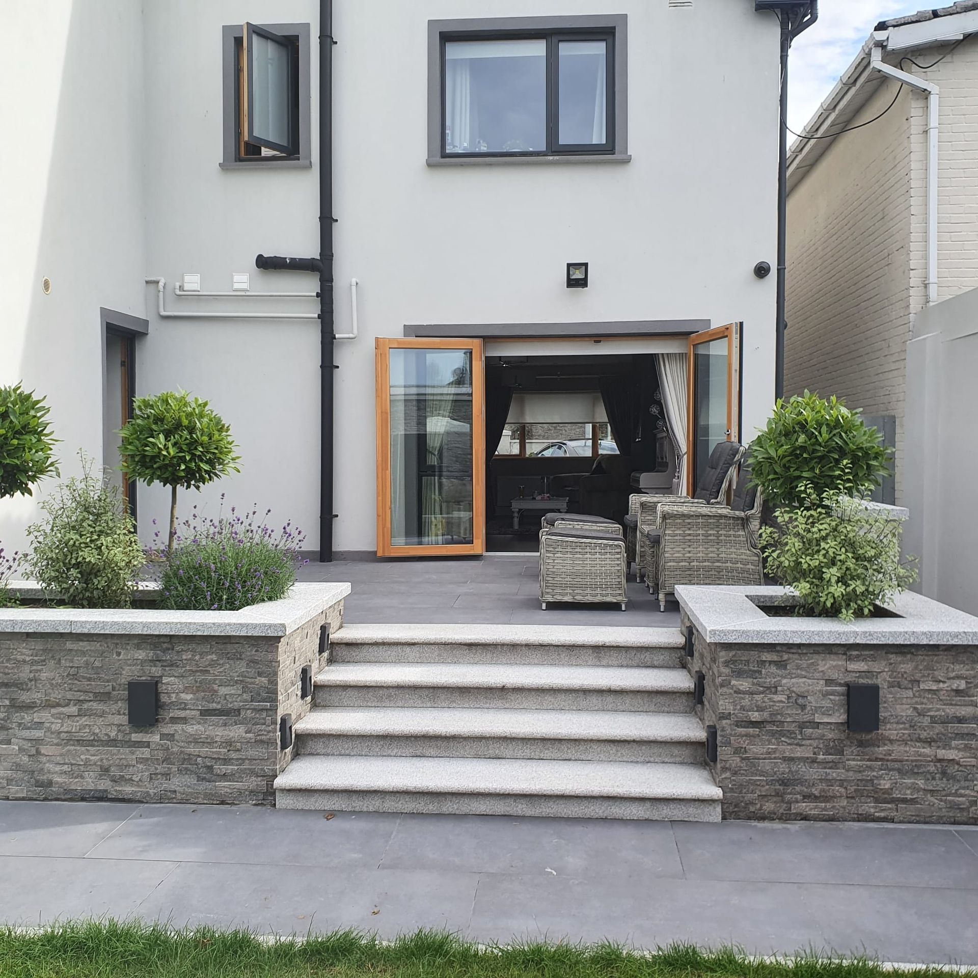 Backyard patio with steps, planters, and a home's rear entrance with open doors.