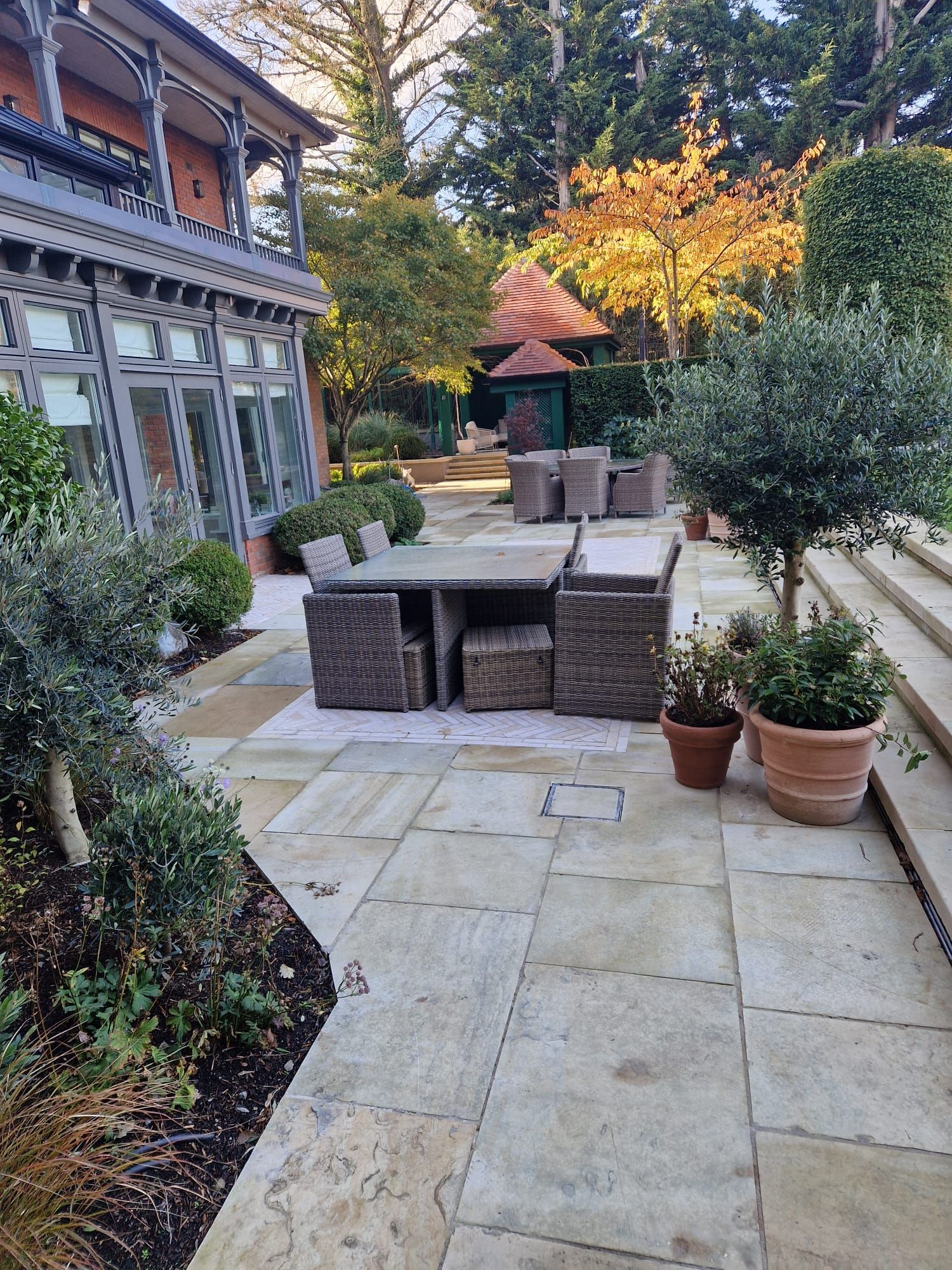 Patio with outdoor furniture, potted plants, and a gazebo, next to a house with a balcony.