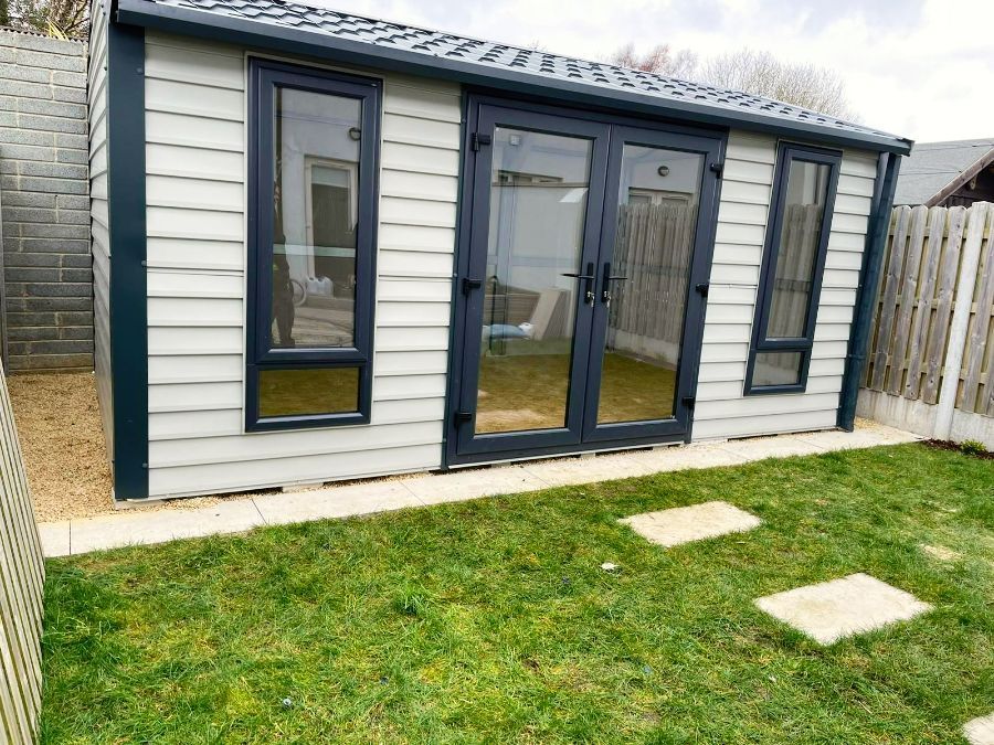 Small backyard shed with gray siding, dark windows and doors, and a small patch of grass.