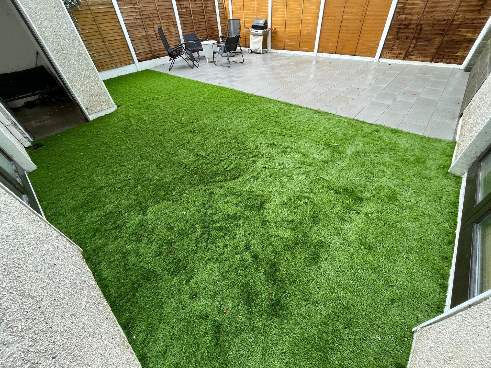 Backyard with artificial green grass and patio furniture on a concrete surface, enclosed by wooden fencing.