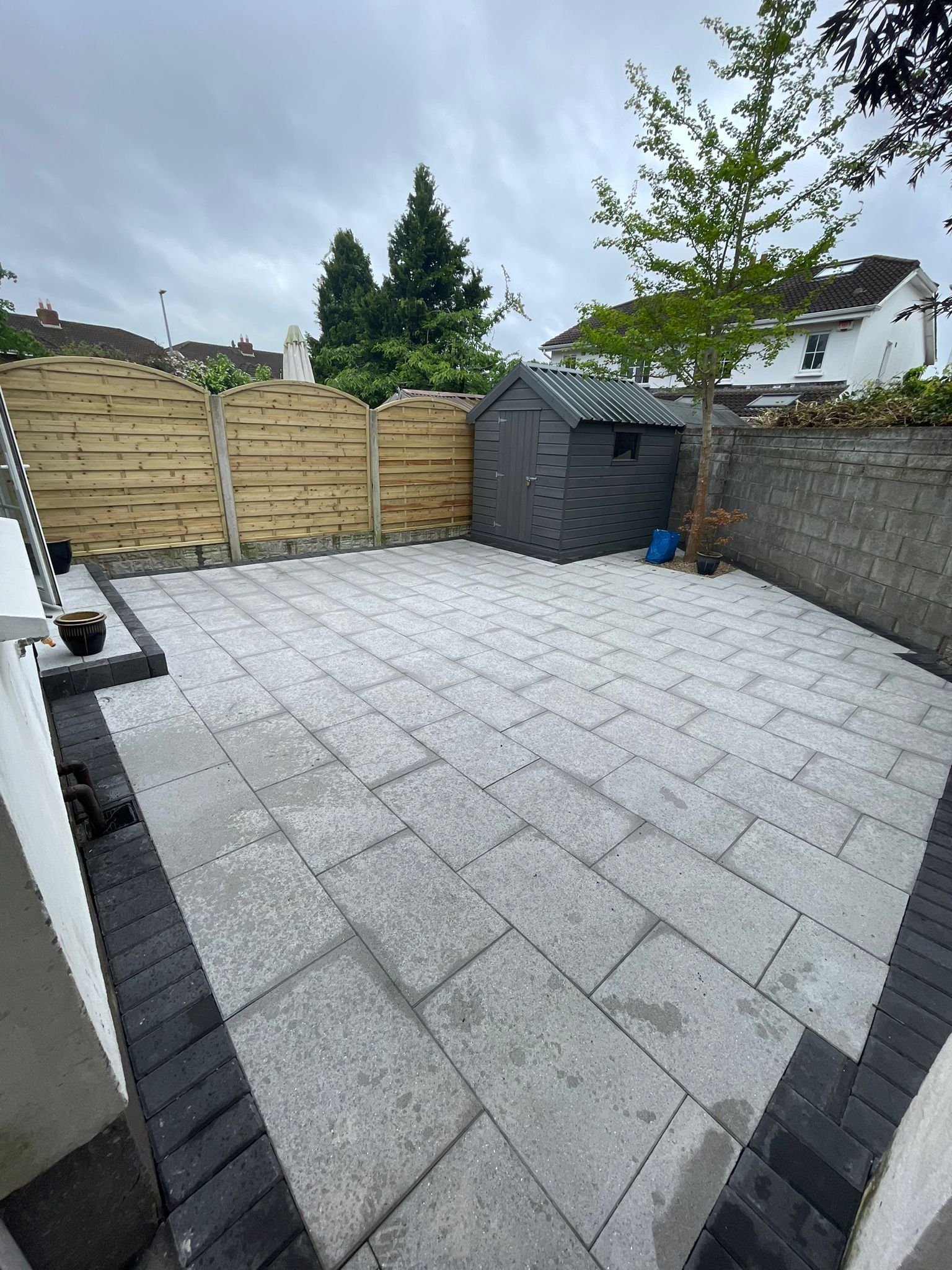 A paved backyard with a small shed and wooden fence.