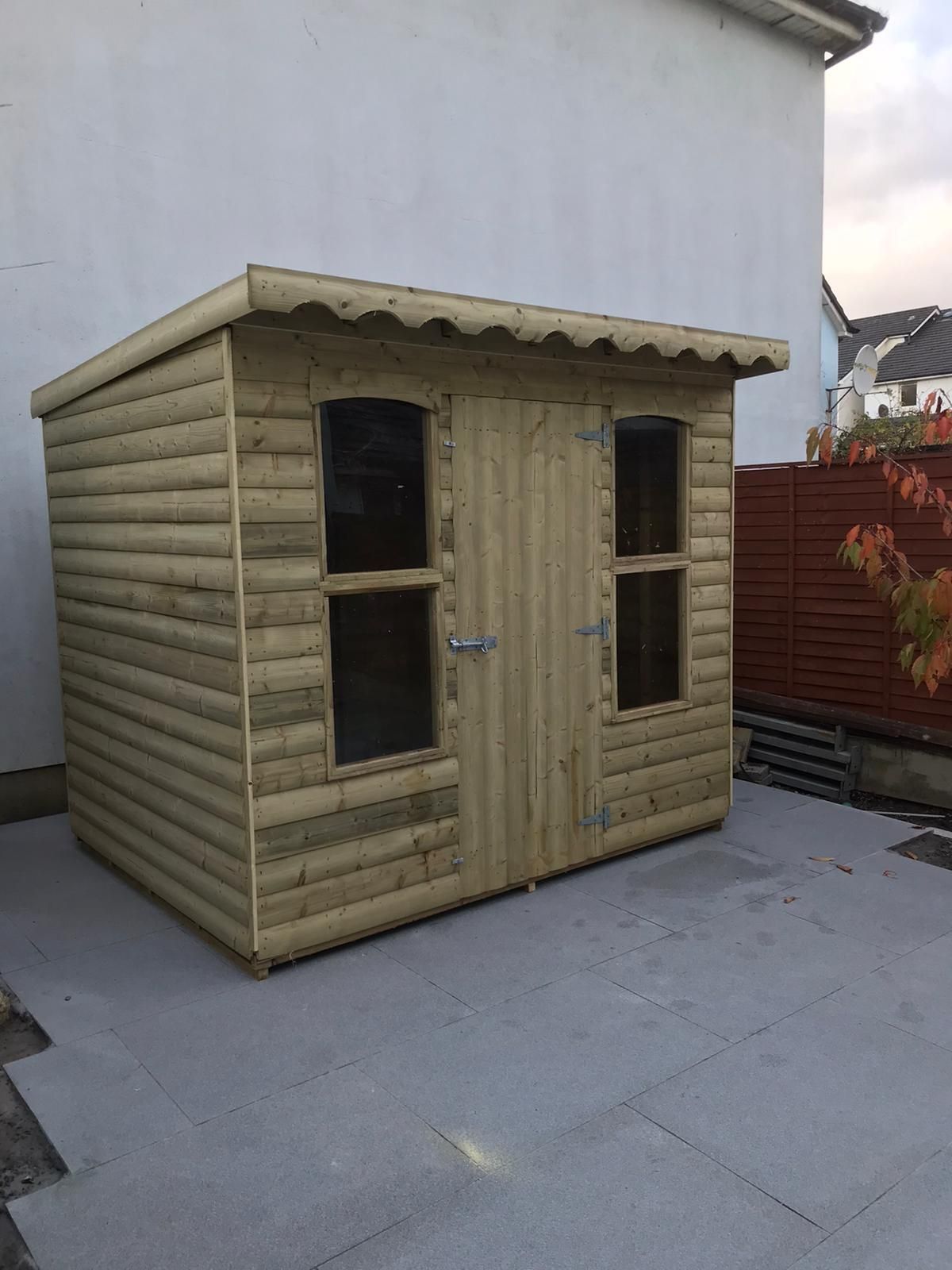 Wooden shed with two windows and a door, on a gray patio.
