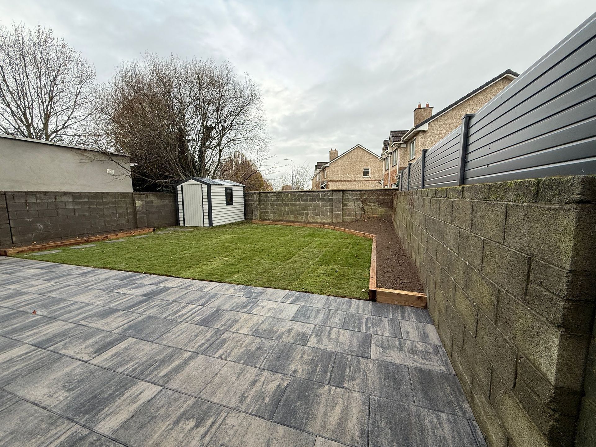 Backyard with paved patio, grass lawn, shed, and brick walls.