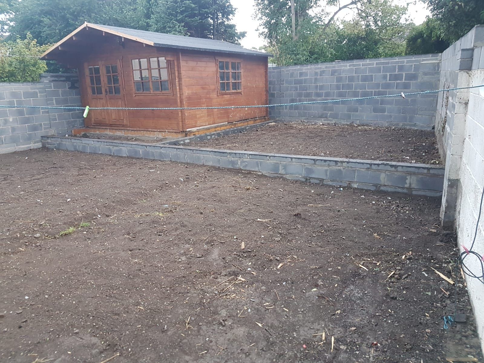 A wooden shed in a dirt yard, enclosed by gray concrete block walls.