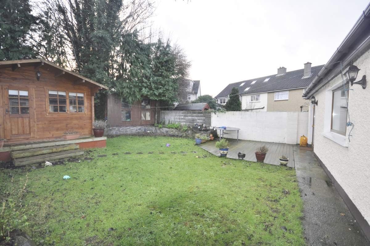 Backyard with shed, grass, patio, and partially visible houses on a cloudy day.