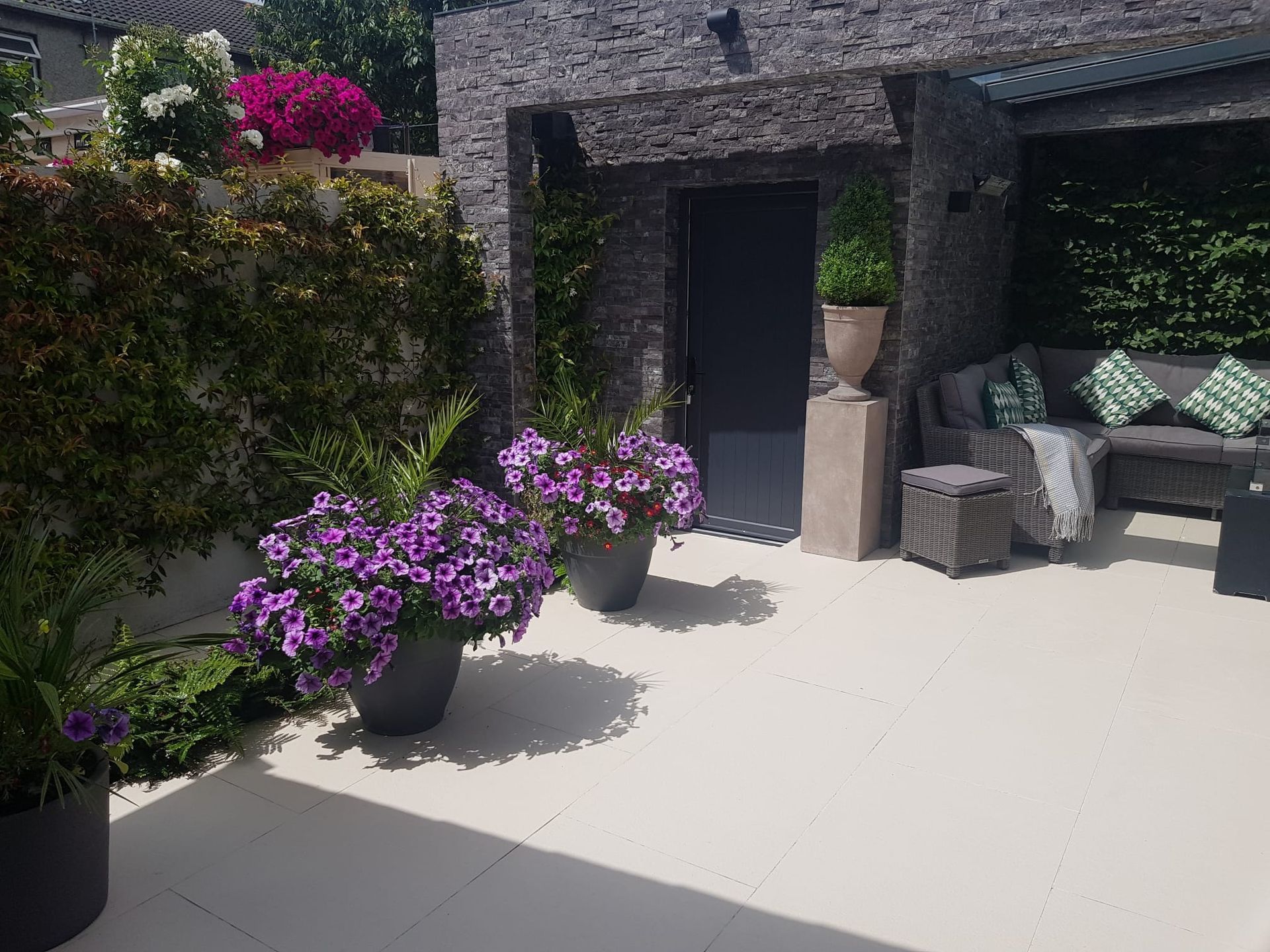 Patio with purple flowers, gray furniture, and a stone wall.