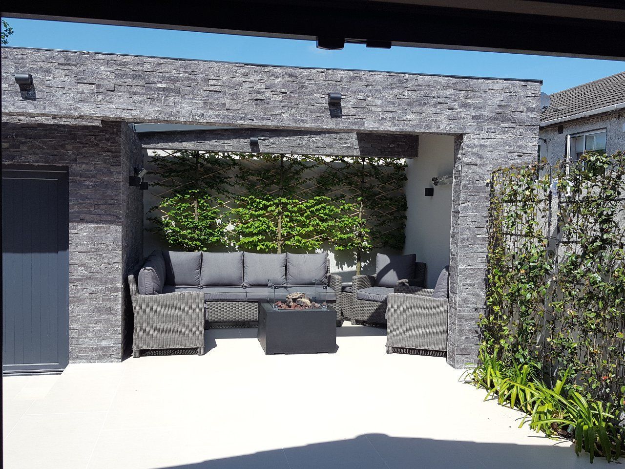 Outdoor patio with gray brick walls, gray wicker furniture, and a green plant wall.