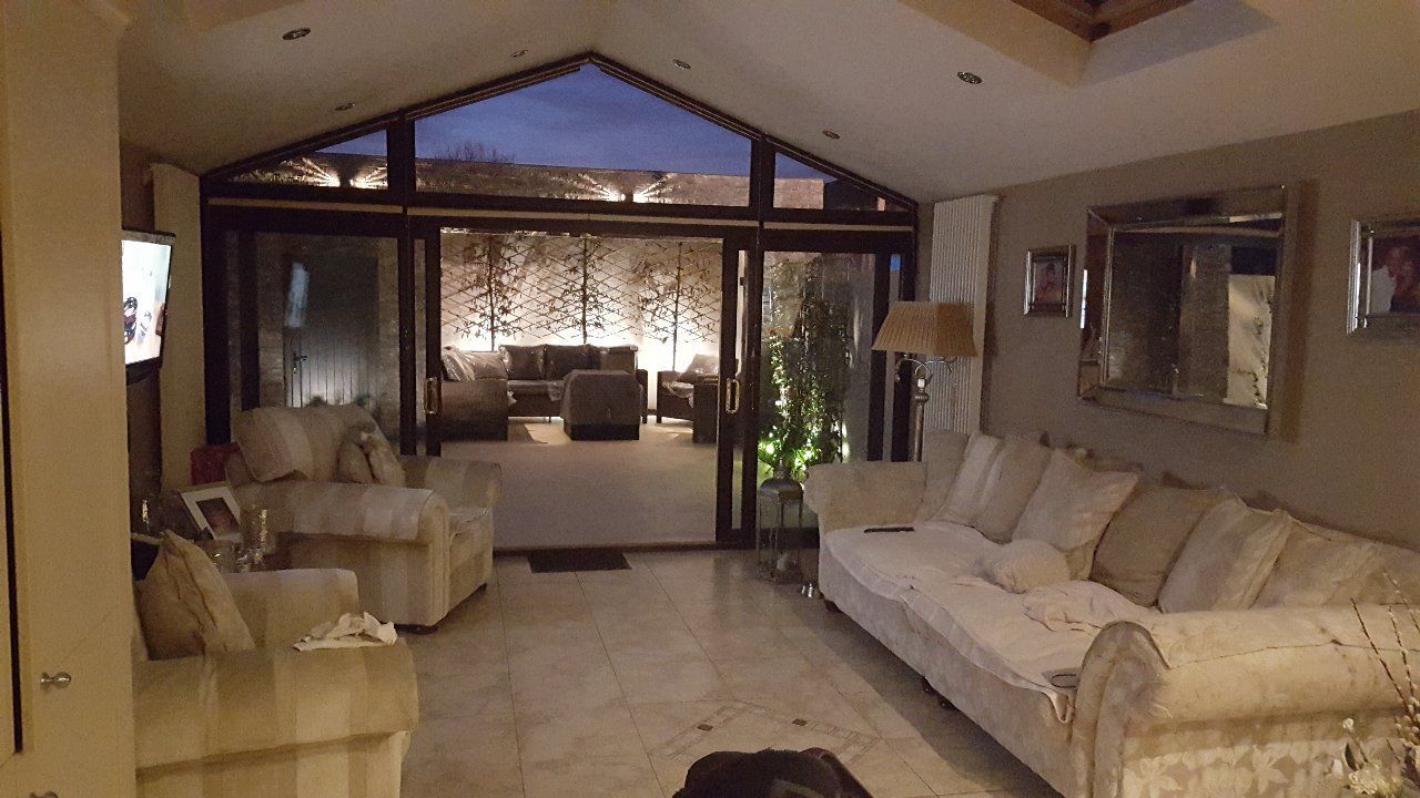 Cozy living room with open doors leading to an outdoor seating area; cream-colored sofas and ambient lighting.