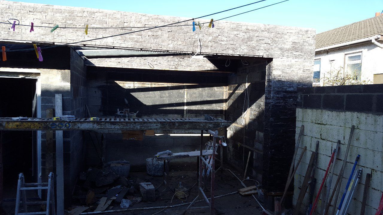 Construction site: exposed beams, unfinished brick walls, scaffolding, tools, bright sunlight, and laundry on a line.
