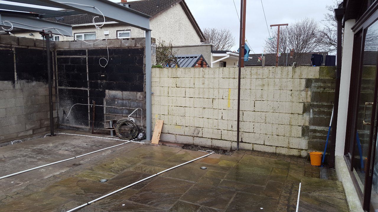 Backyard with concrete block walls, a steel frame, and wet paving stones.