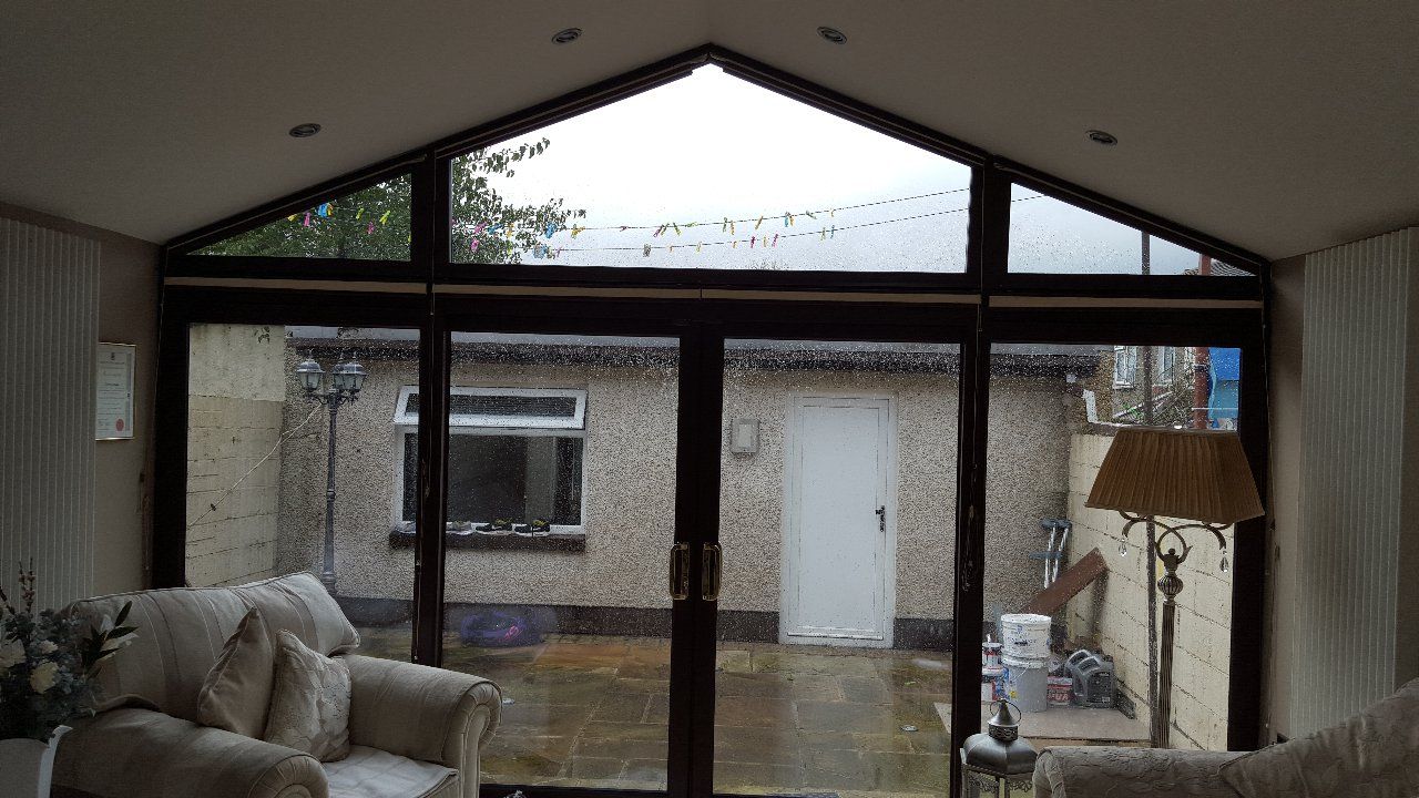 Interior view of a sunroom with large windows overlooking a courtyard. A sofa and lamp are visible inside.