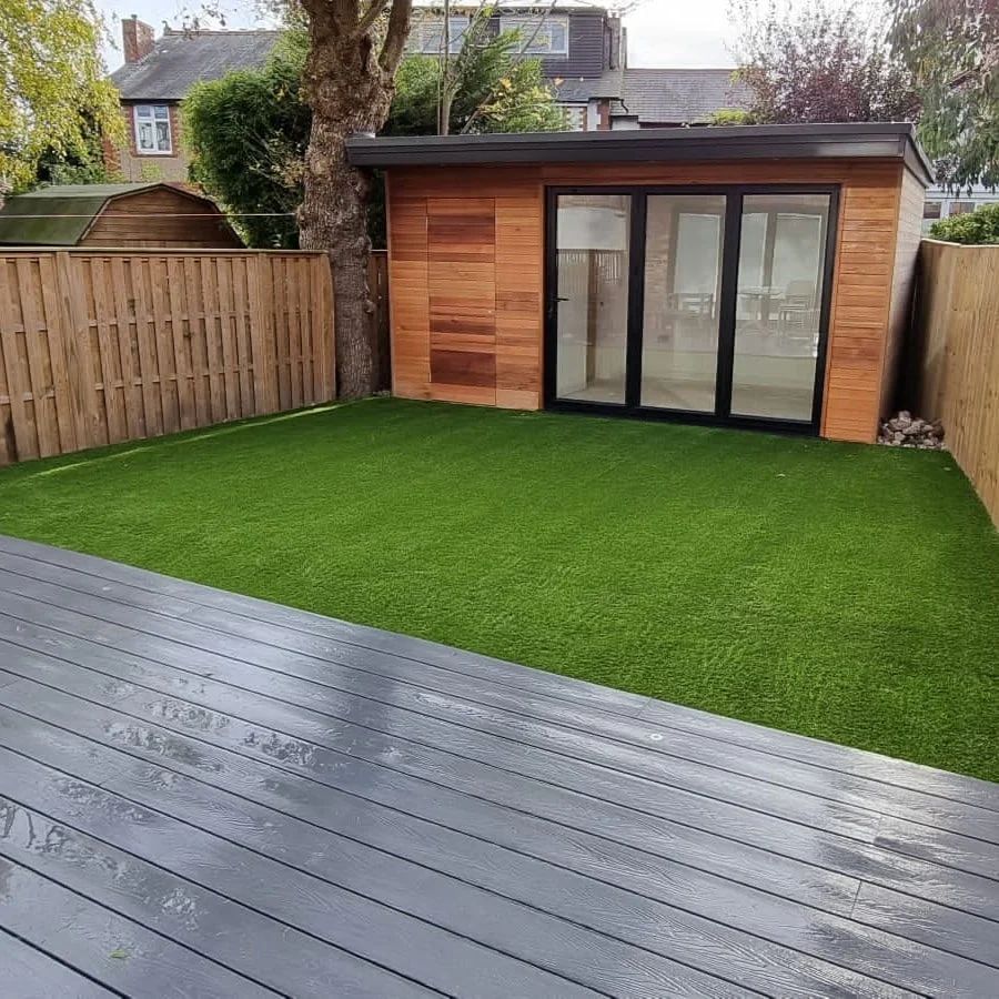 Backyard with wooden deck, artificial grass, and a wooden shed with glass doors.