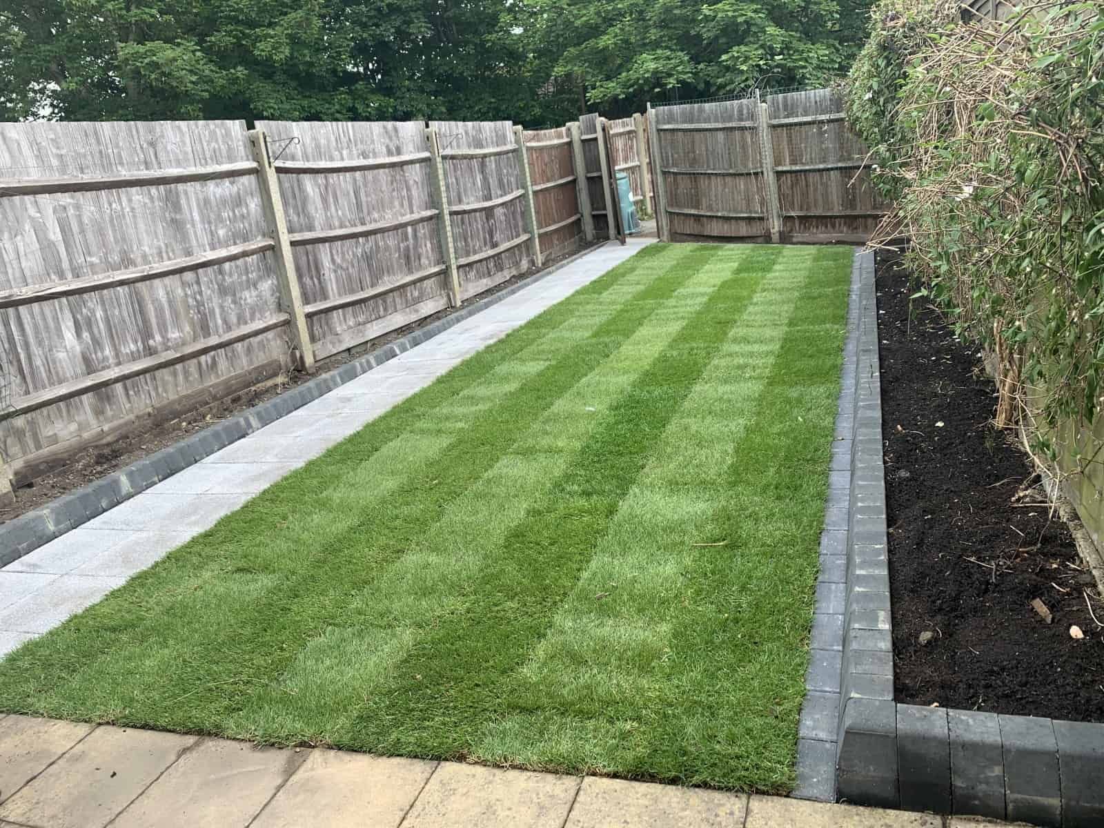 Well-manicured lawn bordered by paved walkways and wooden fence.