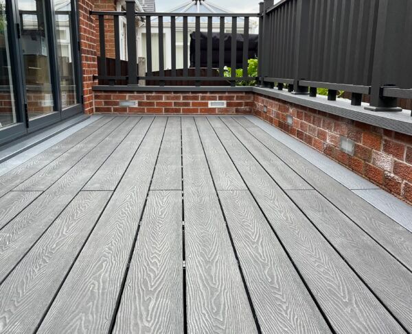 Gray composite deck with brick wall and black railing.