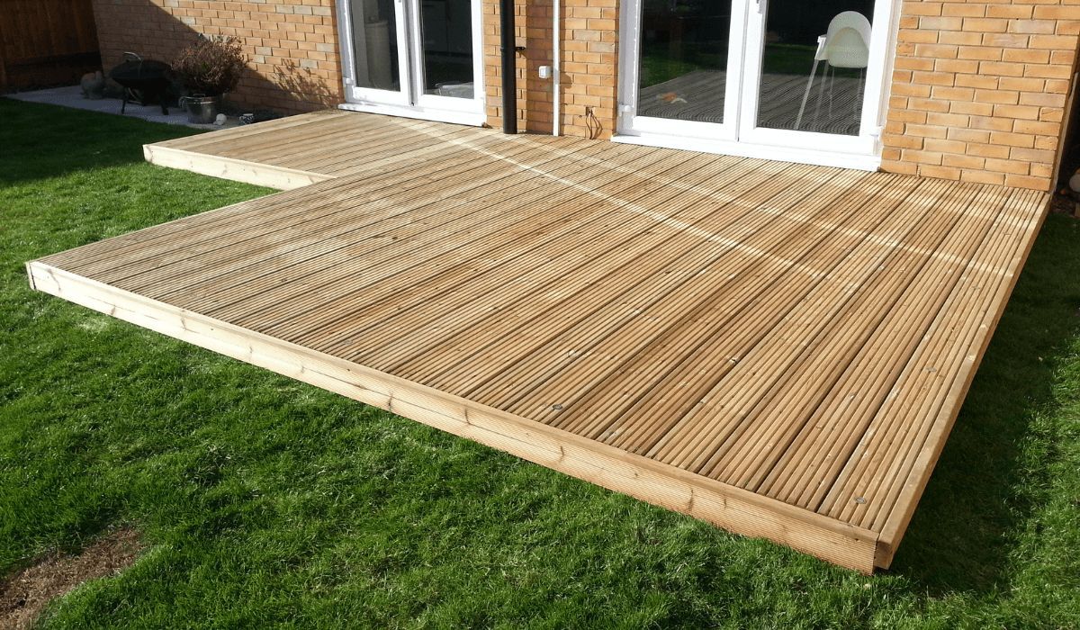 Wooden deck extension on green grass in front of a brick building with white doors.