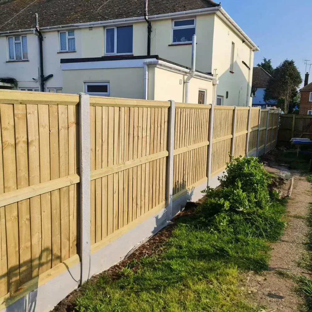 Wooden fence with concrete posts bordering a backyard with grass and a house.