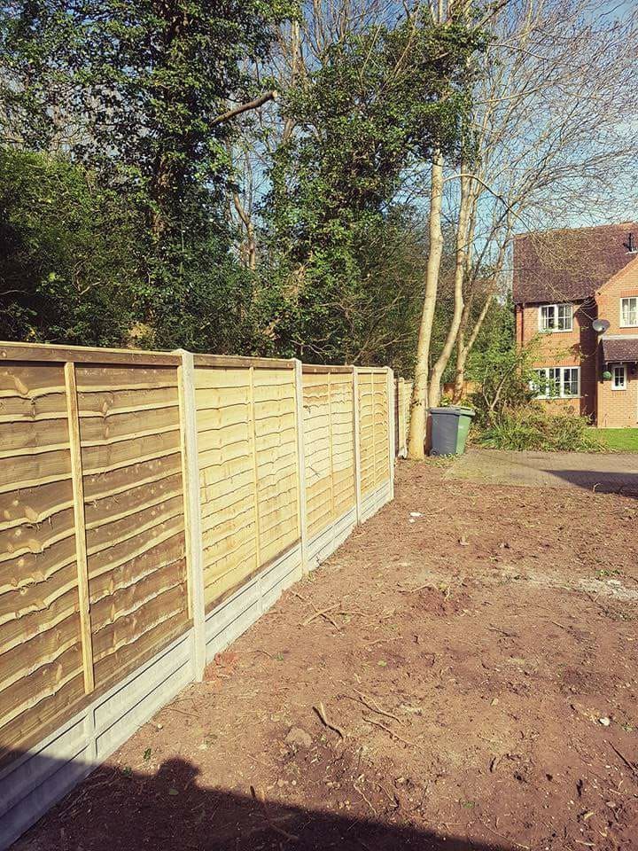 Wooden fence with concrete base in a yard, trees and a house in the background.
