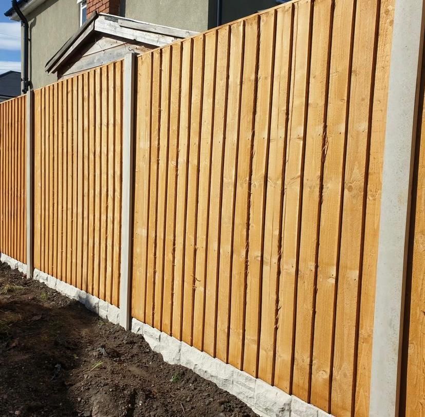 Wooden fence with vertical planks, concrete posts and base.