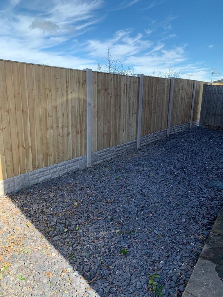 Wooden fence with concrete posts and gravel ground, under a blue sky.