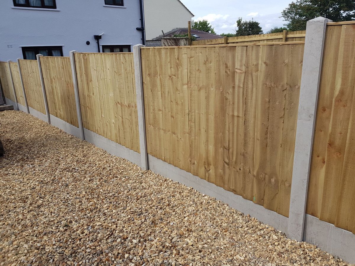 Wooden fence with concrete posts and base in a gravel yard.