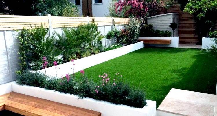Modern backyard with green turf, white borders, wooden benches, and lush plants.