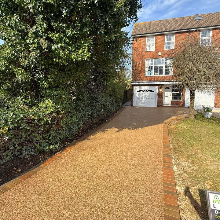 Driveway of a two-story brick house with a gravel surface, bordered by a hedge and brick.