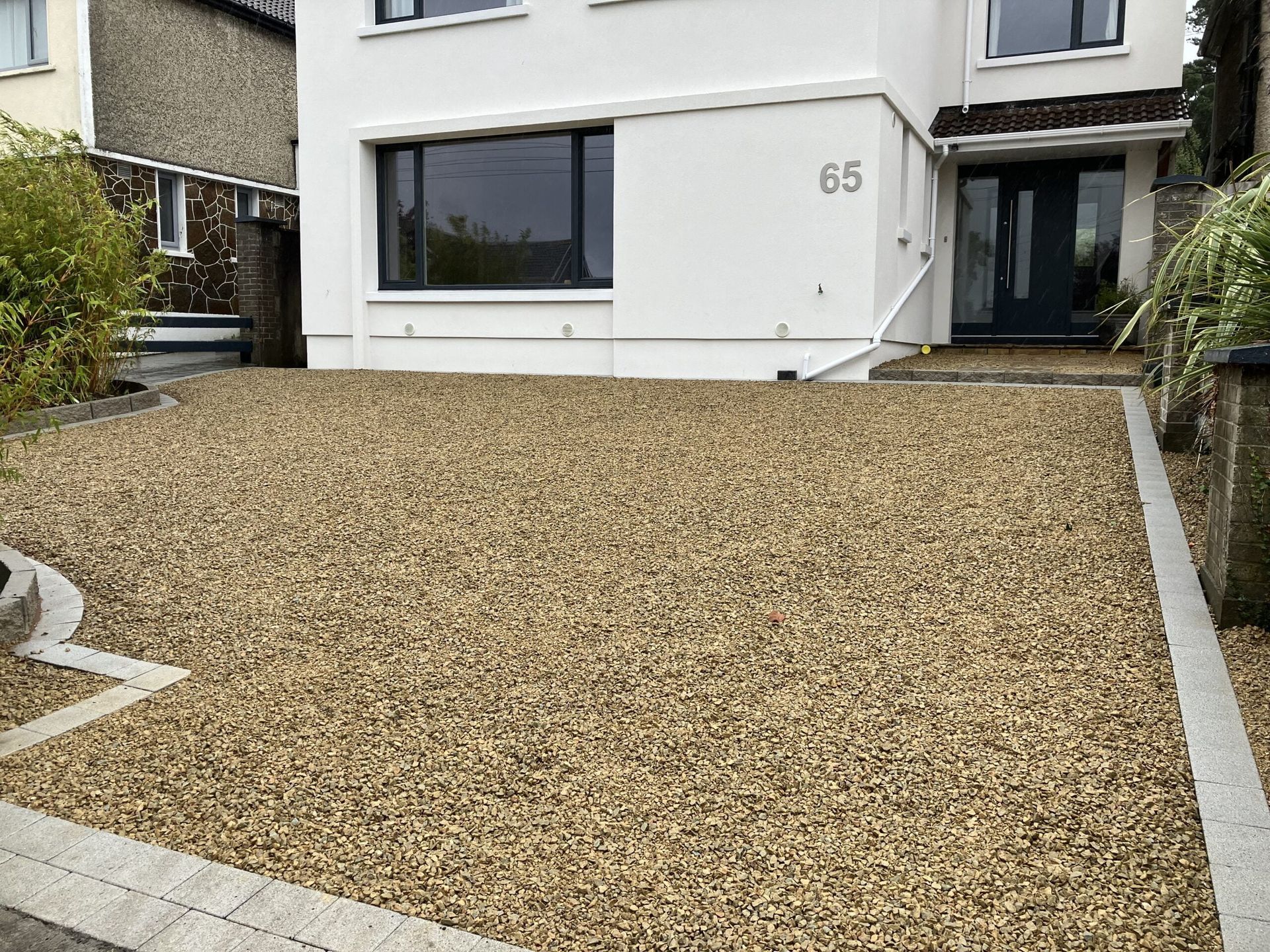 Gravel driveway leading to a white house with a black door and window; address is 65.