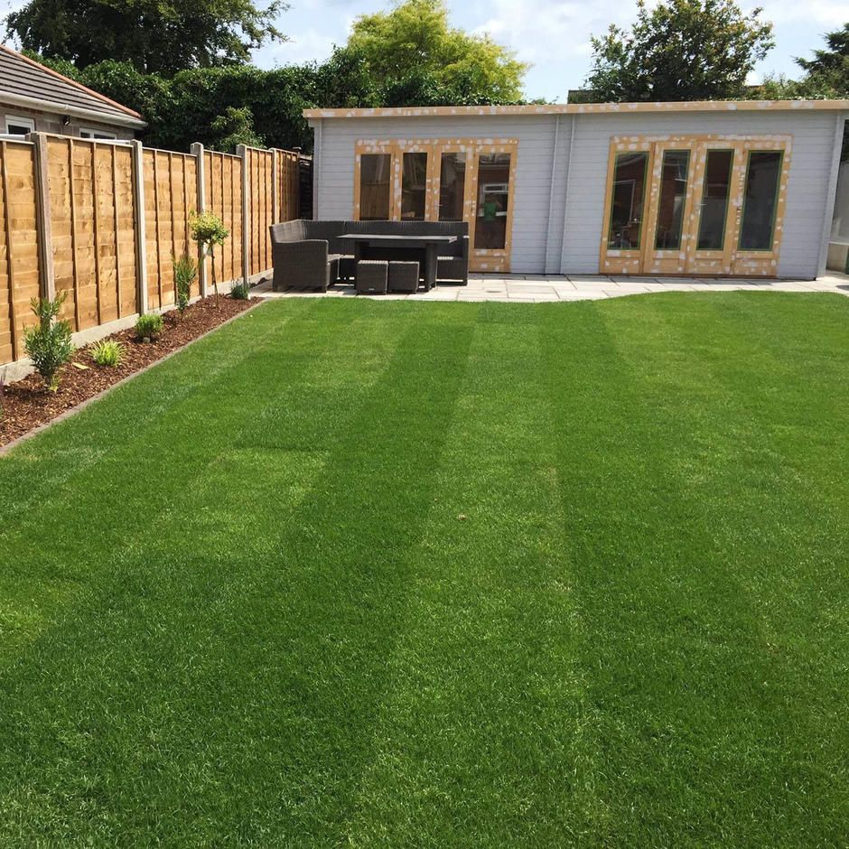 Well-manicured green lawn with a wooden shed and a brown fence.