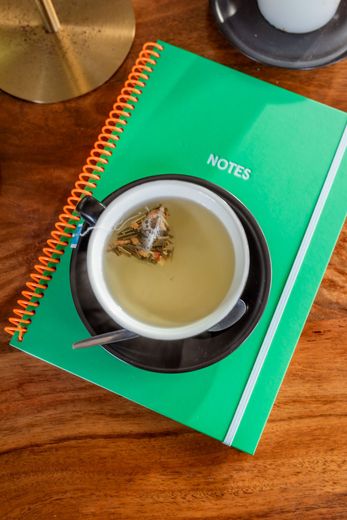 Cup of tea with loose leaf, on saucer and green notebook on a wooden table.