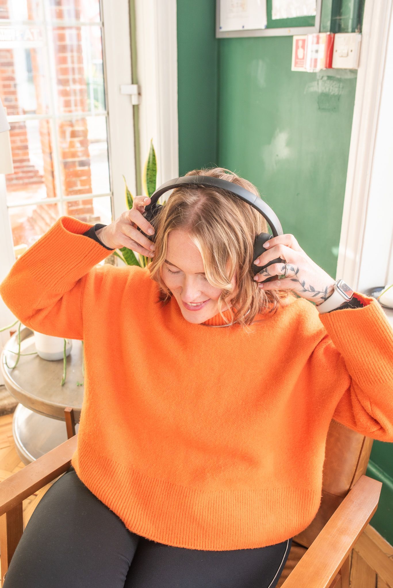 Person in orange sweater putting on headphones indoors.