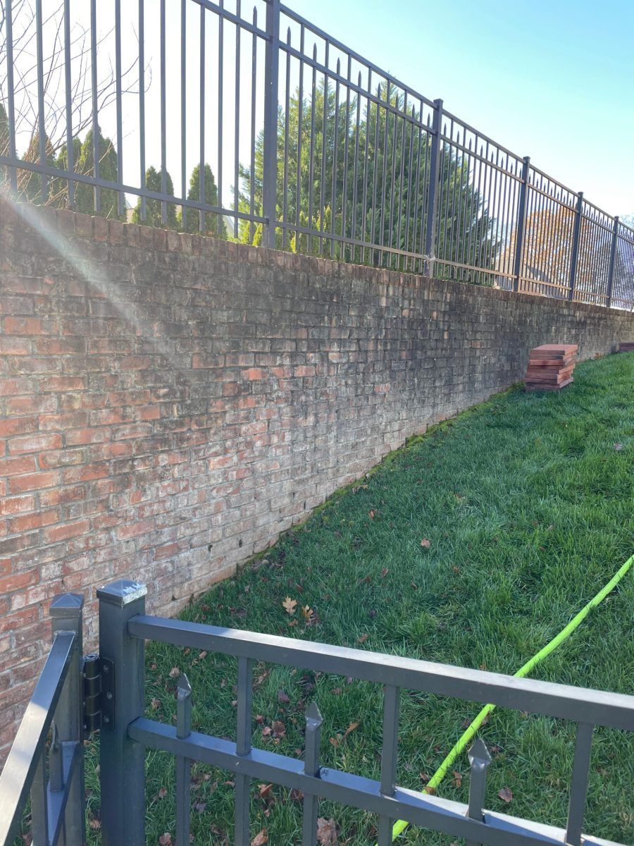 A fence is spraying water on a brick wall in a yard.