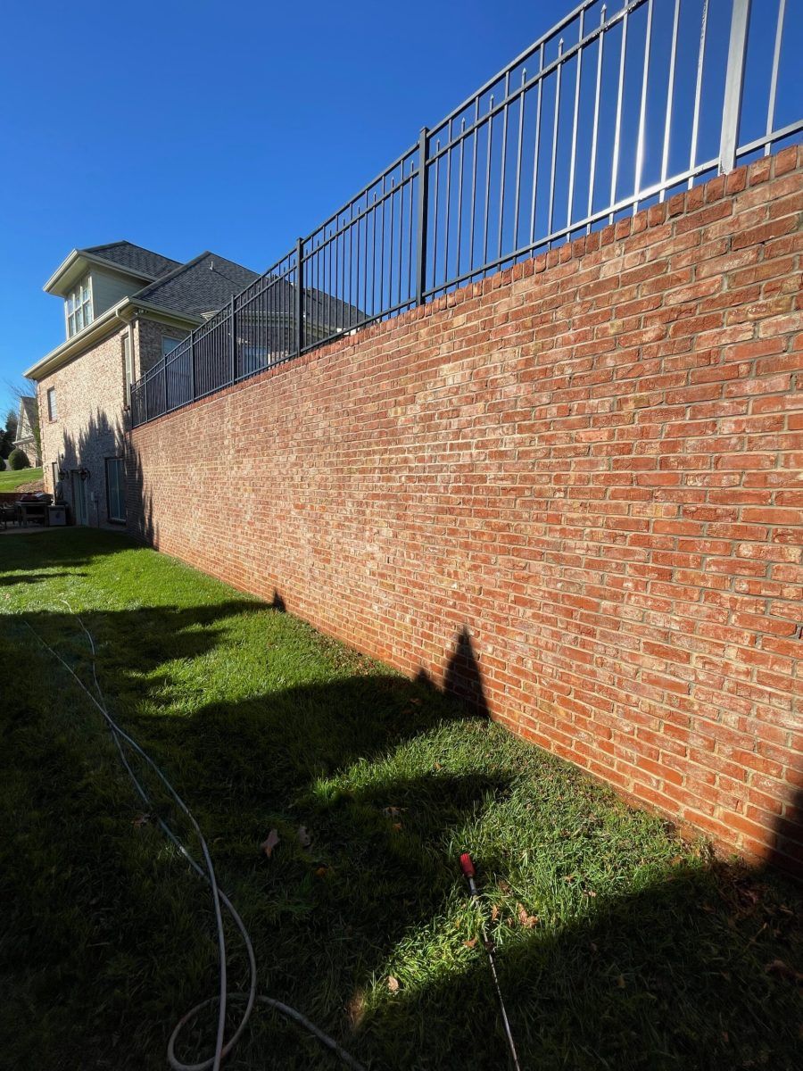 A large brick wall is surrounded by grass and a fence.