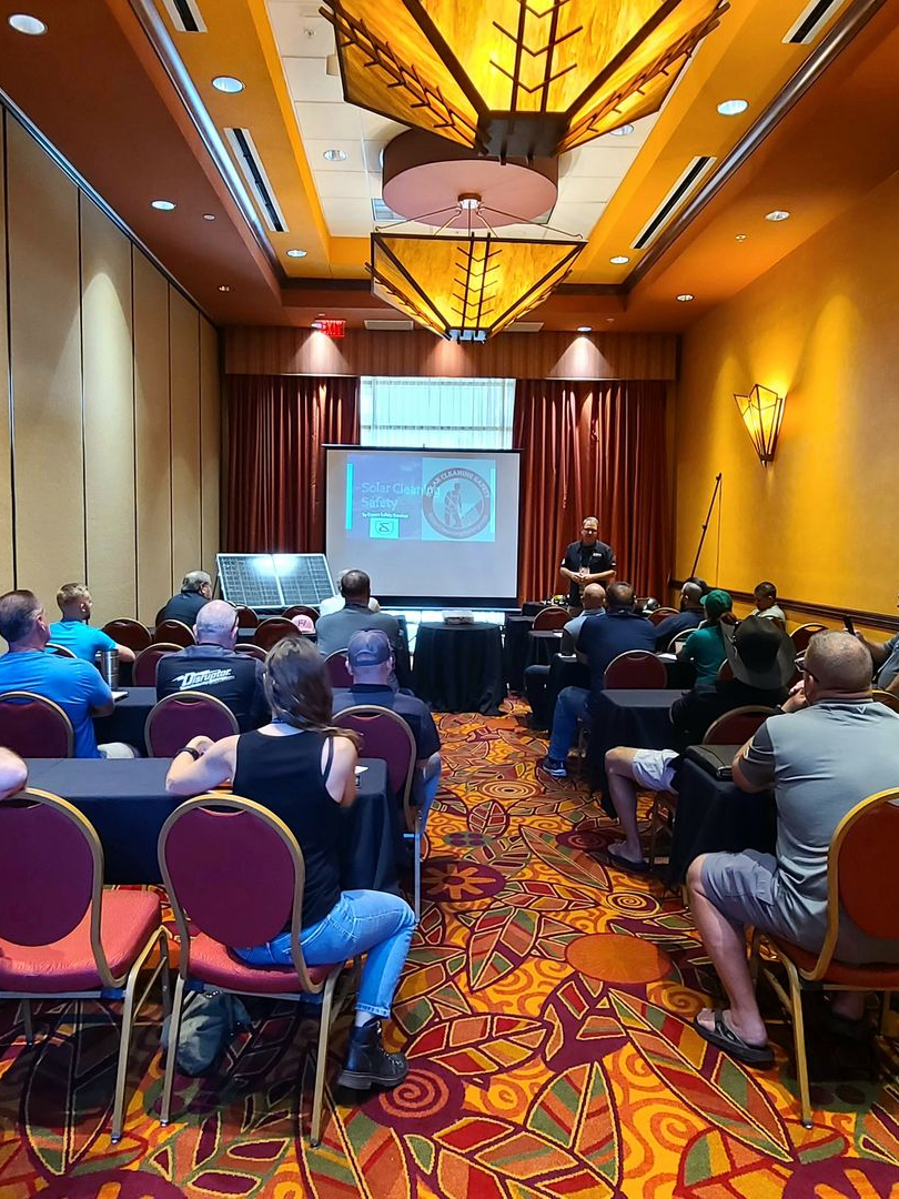 Conference attendees seated in a hotel ballroom facing a projected presentation screen