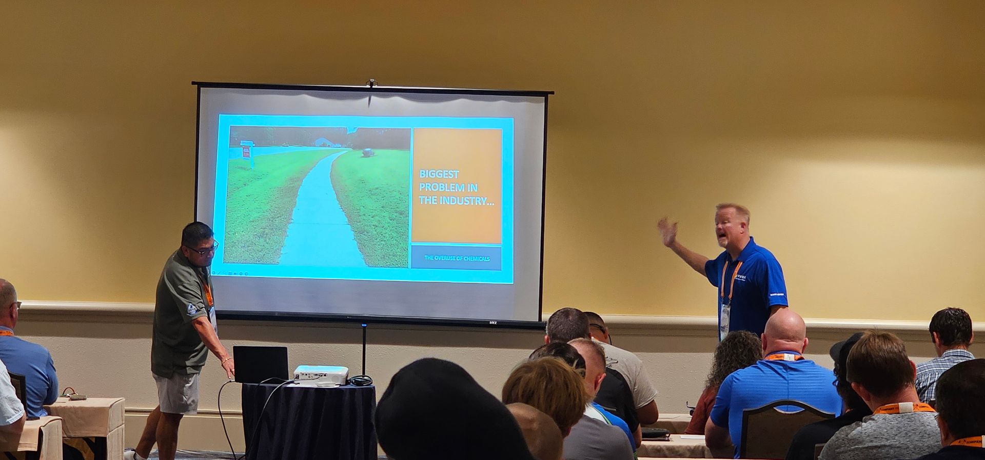 Two presenters at a conference show a slide with a road map on a projection screen.