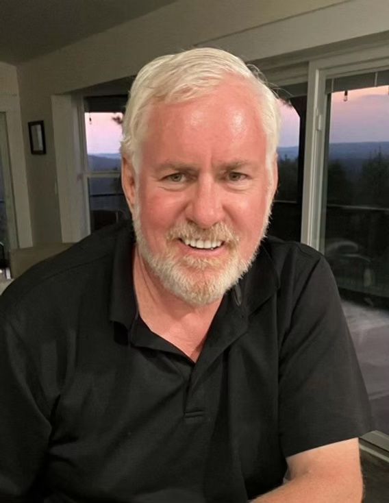 Smiling man in a black polo shirt indoors by a window at sunset